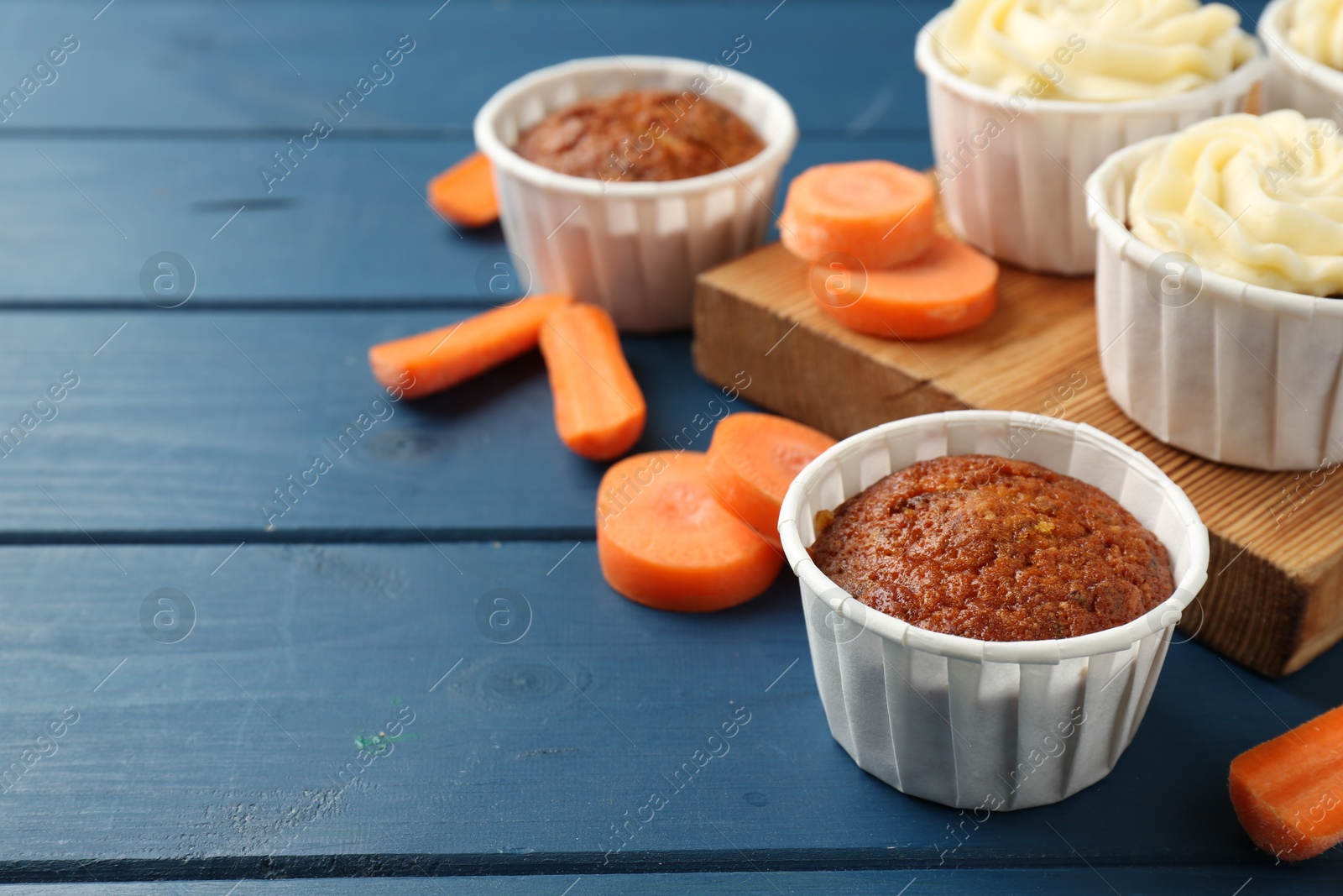 Photo of Delicious carrot muffins and fresh vegetables on blue wooden table, closeup. Space for text