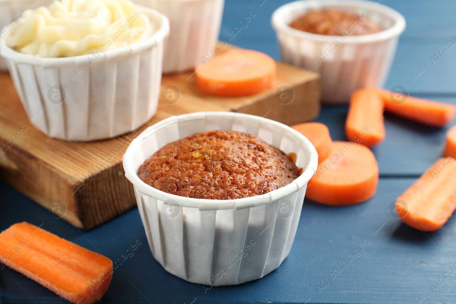 Photo of Delicious carrot muffins and fresh vegetables on blue wooden table, closeup