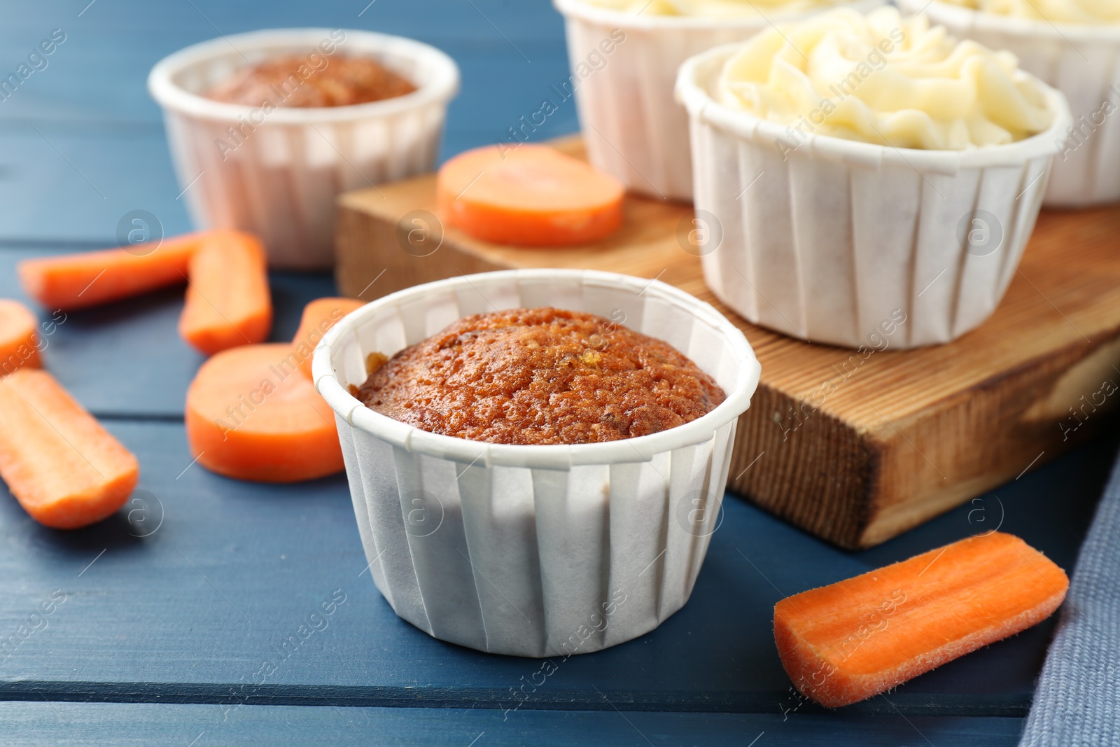 Photo of Delicious carrot muffins and fresh vegetables on blue wooden table, closeup