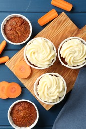 Photo of Delicious carrot muffins and fresh vegetables on blue wooden table, flat lay