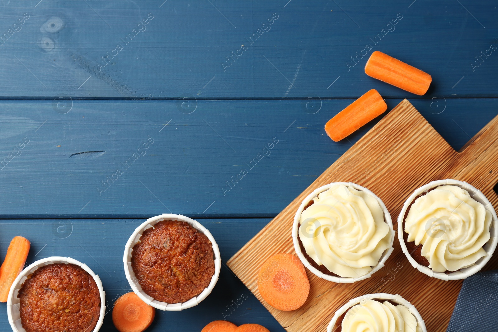 Photo of Delicious carrot muffins and fresh vegetables on blue wooden table, flat lay. Space for text