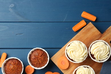 Photo of Delicious carrot muffins and fresh vegetables on blue wooden table, flat lay. Space for text