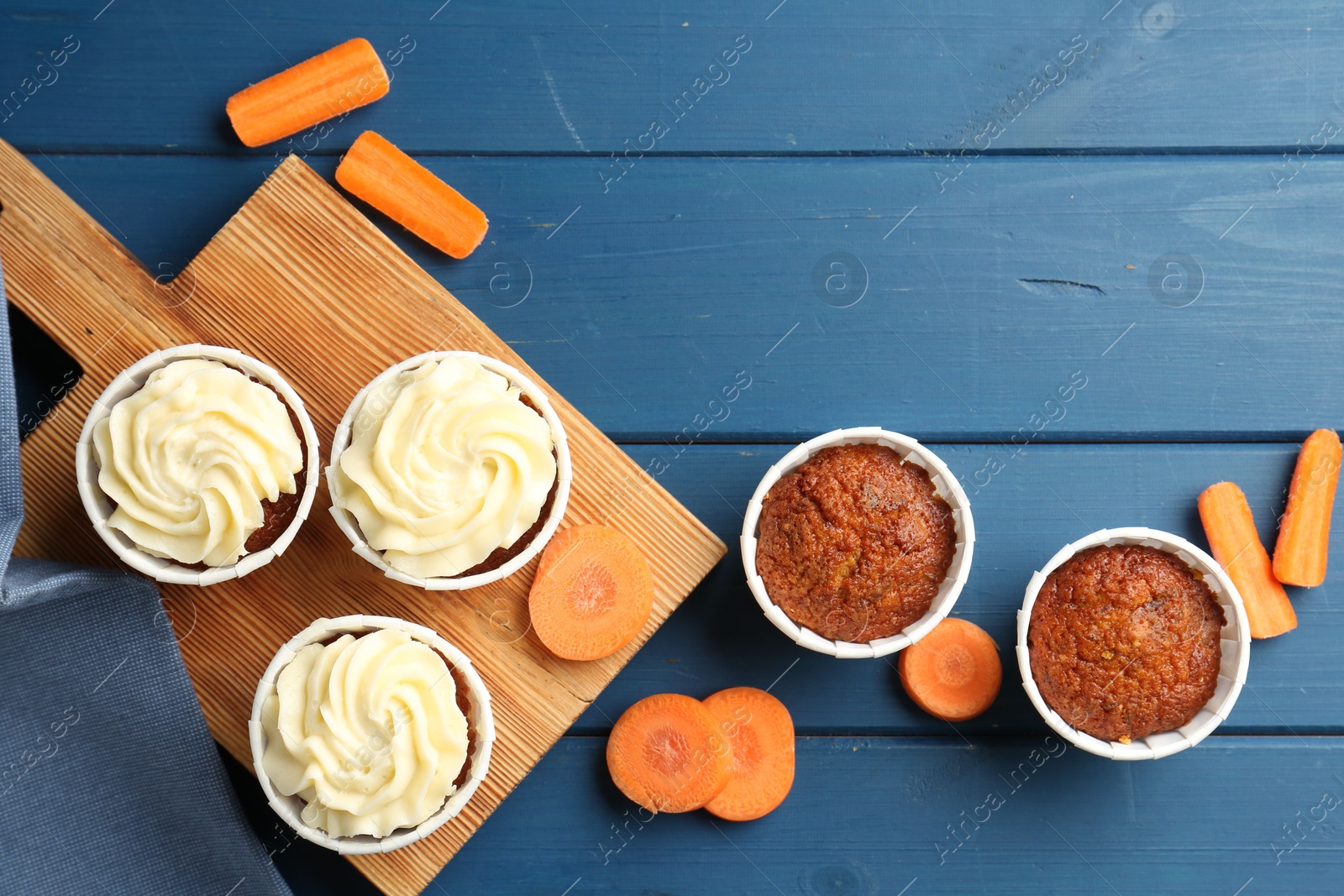 Photo of Delicious carrot muffins and fresh vegetables on blue wooden table, flat lay. Space for text