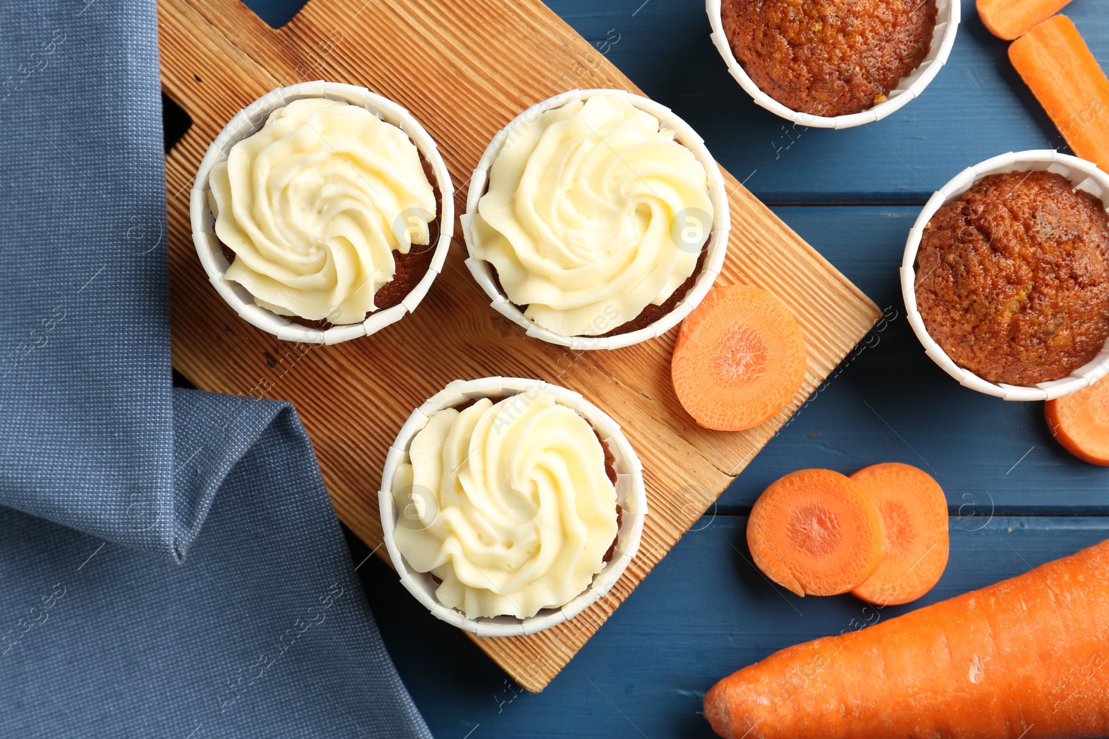 Photo of Delicious carrot muffins and fresh vegetables on blue wooden table, flat lay