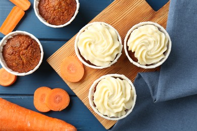 Photo of Delicious carrot muffins and fresh vegetables on blue wooden table, flat lay