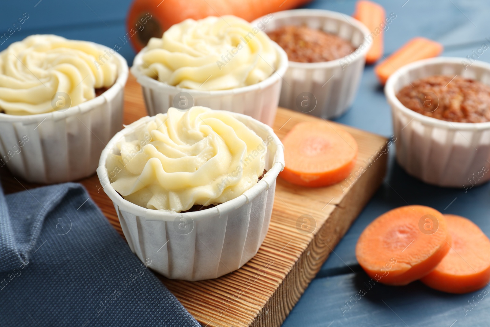 Photo of Delicious carrot muffins and fresh vegetables on blue wooden table, closeup