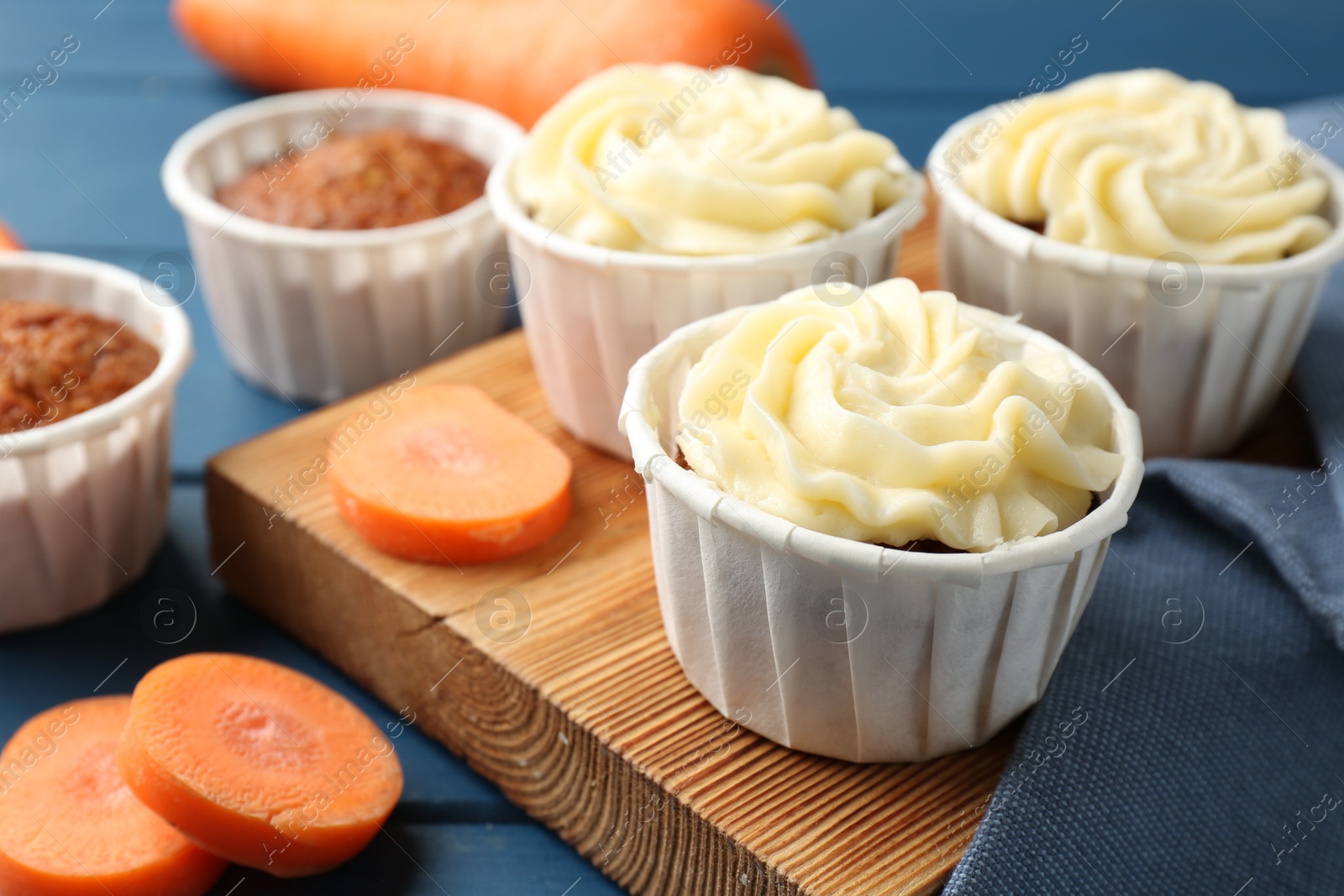 Photo of Delicious carrot muffins and fresh vegetables on blue wooden table, closeup