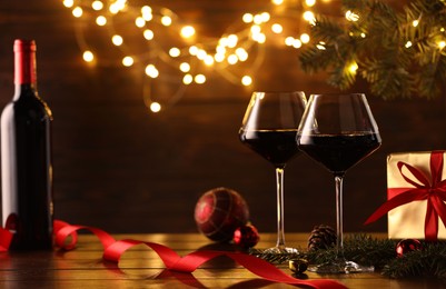 Photo of Red wine and beautiful Christmas decor on wooden table against blurred festive lights. Space for text