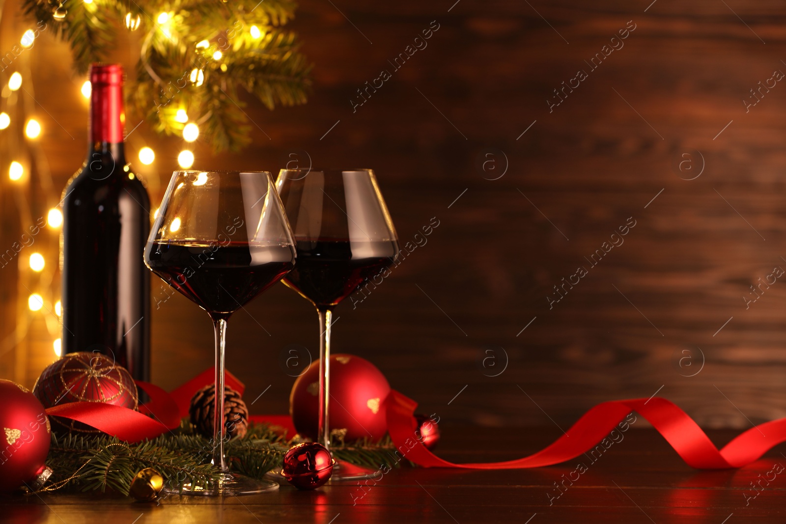 Photo of Red wine and beautiful Christmas decor on wooden table against blurred festive lights. Space for text