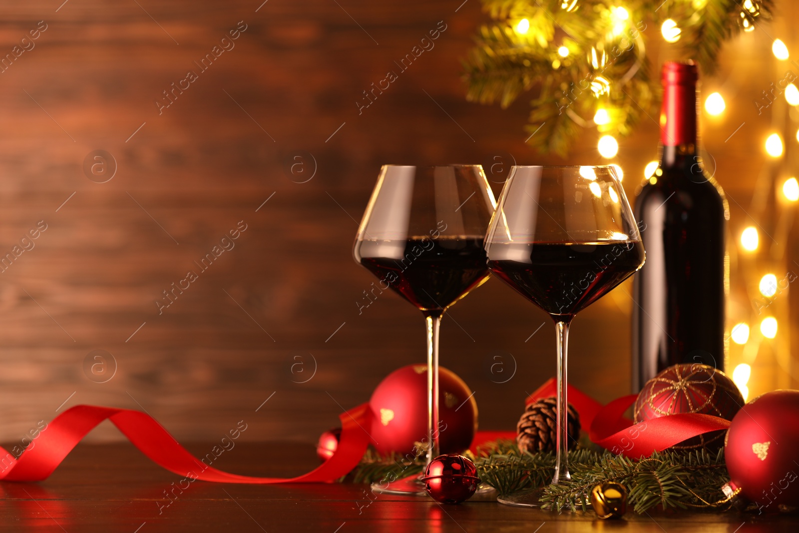 Photo of Red wine and beautiful Christmas decor on wooden table against blurred festive lights. Space for text