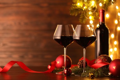 Photo of Red wine and beautiful Christmas decor on wooden table against blurred festive lights. Space for text