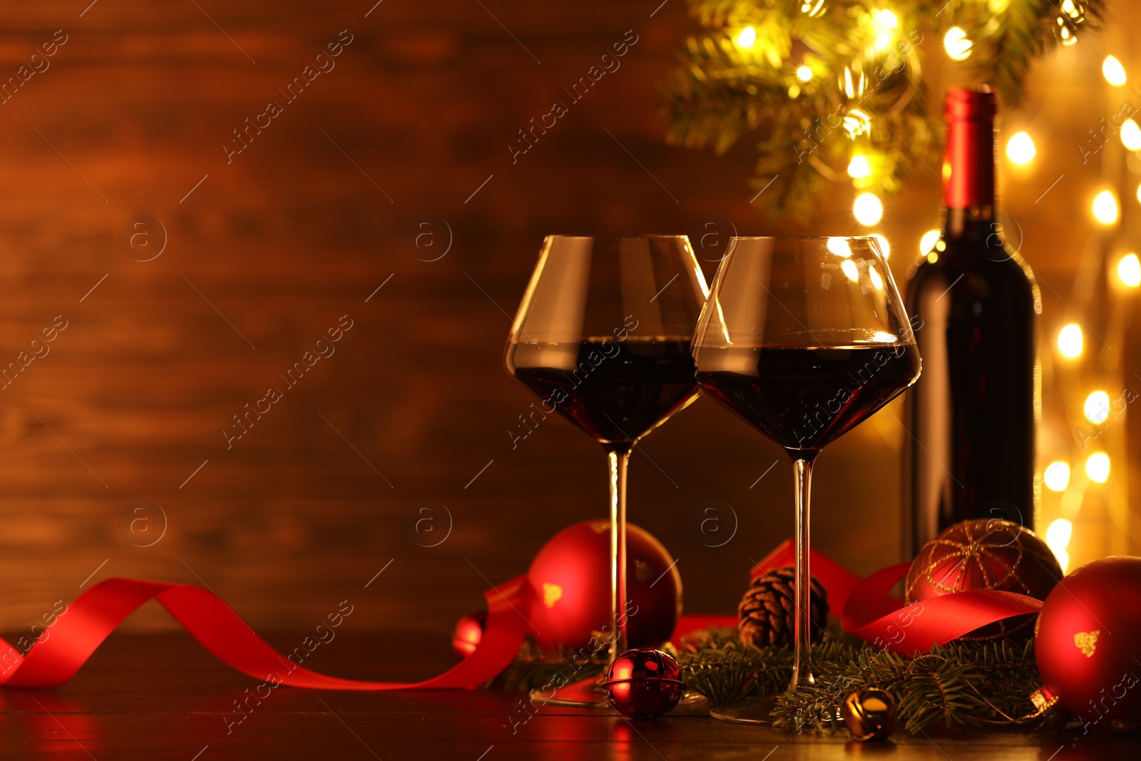 Photo of Red wine and beautiful Christmas decor on wooden table against blurred festive lights. Space for text