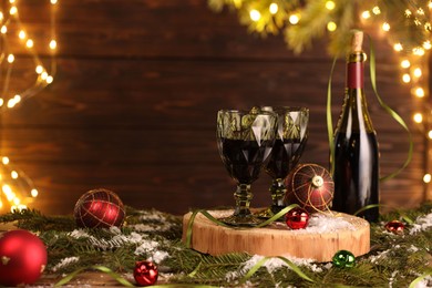 Photo of Red wine and beautiful Christmas decor on wooden table against blurred festive lights. Space for text