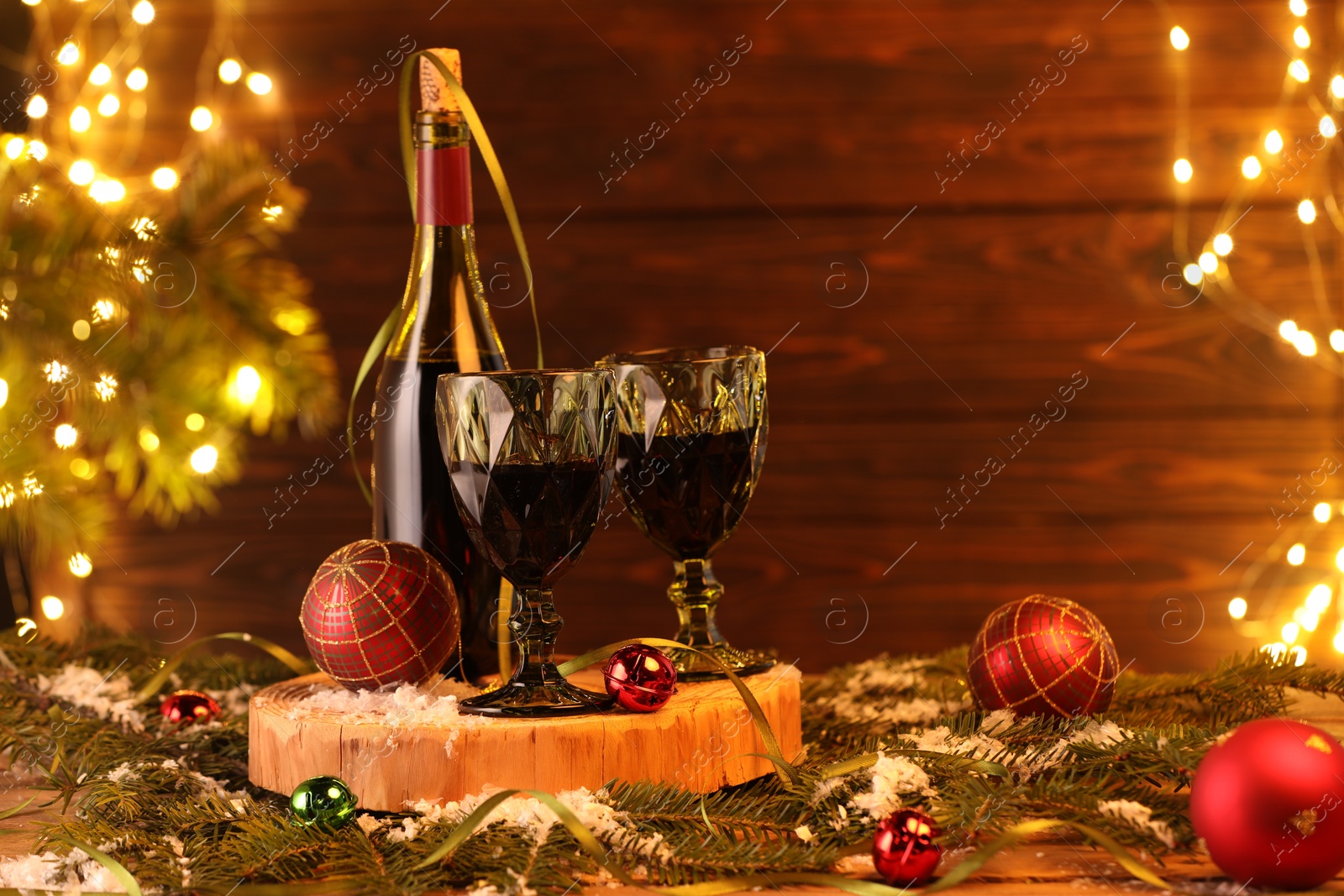 Photo of Red wine and beautiful Christmas decor on wooden table against blurred festive lights. Space for text