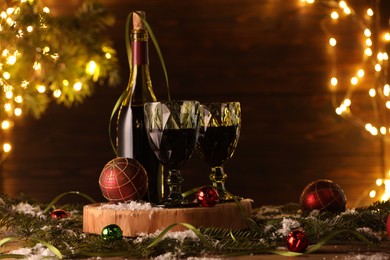 Photo of Red wine and beautiful Christmas decor on wooden table against blurred festive lights