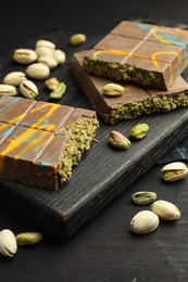 Photo of Pieces of Dubai chocolate bars with pistachios and knafeh on black wooden table, closeup