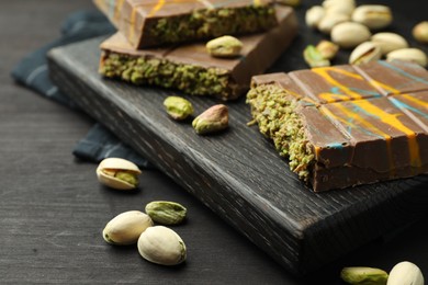 Photo of Pieces of Dubai chocolate bars with pistachios and knafeh on black wooden table, closeup