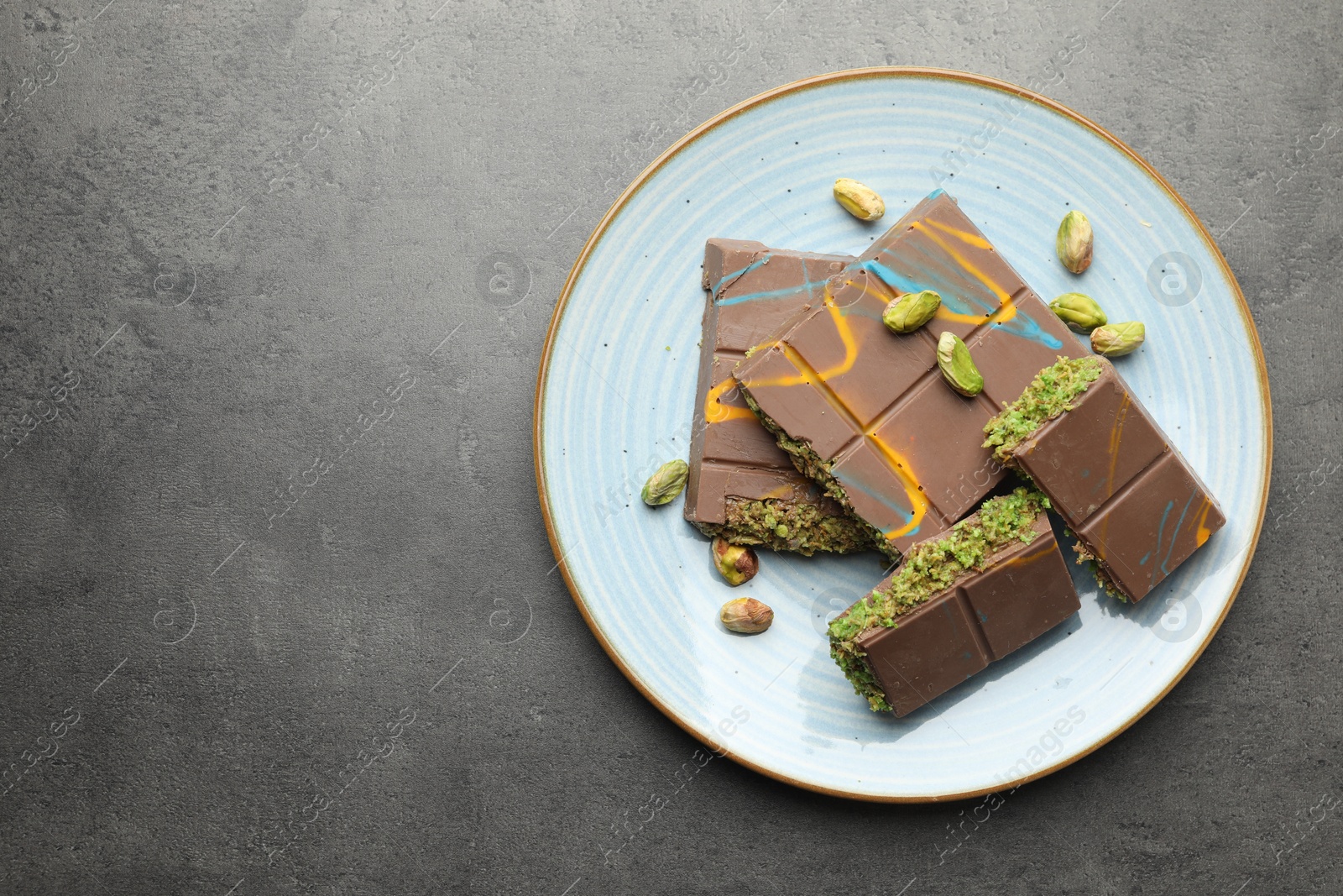 Photo of Pieces of Dubai chocolate bar with pistachios and knafeh on grey table, top view. Space for text