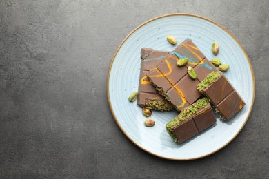 Photo of Pieces of Dubai chocolate bar with pistachios and knafeh on grey table, top view. Space for text