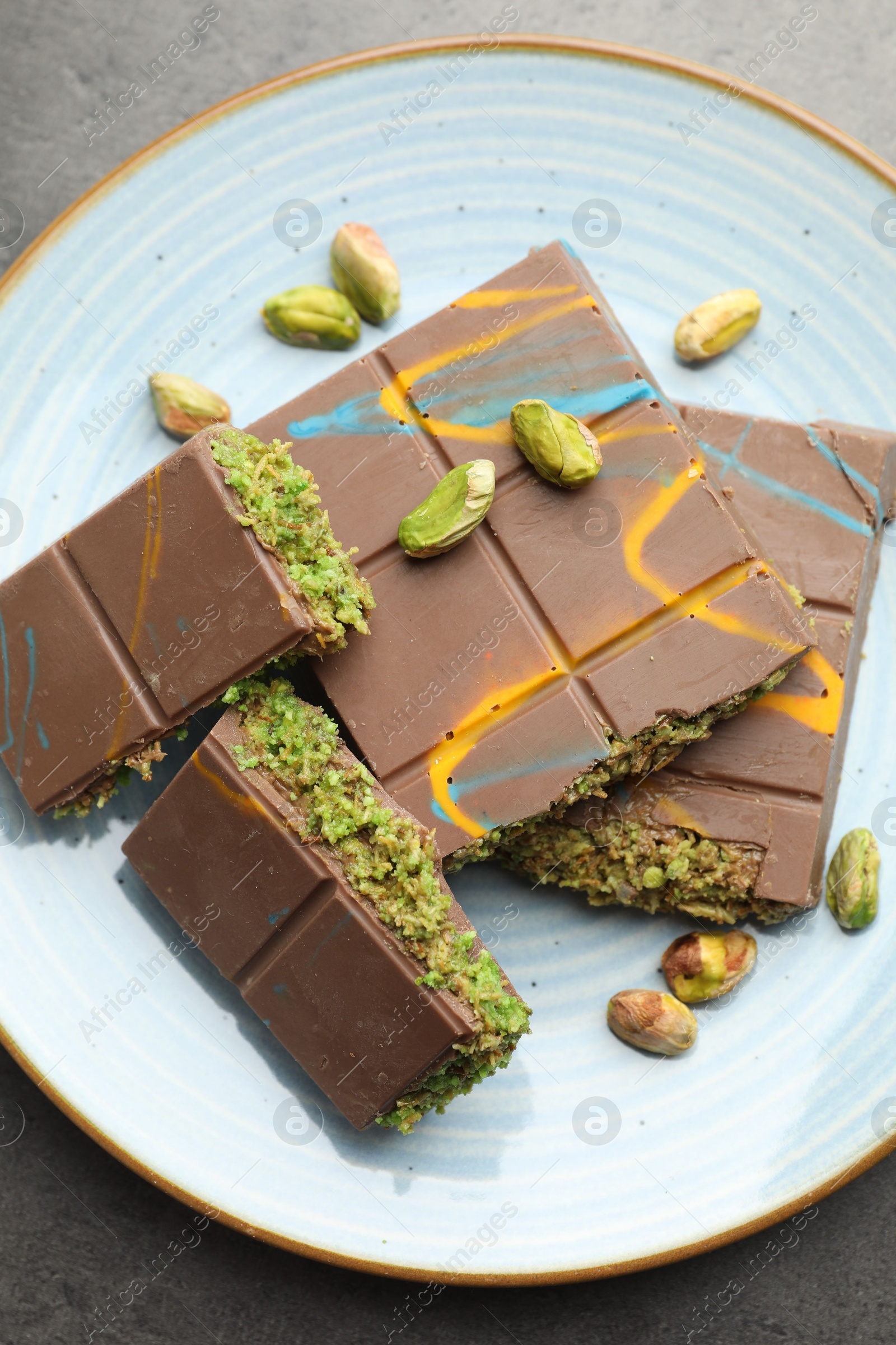 Photo of Pieces of Dubai chocolate bar with pistachios and knafeh on grey table, top view