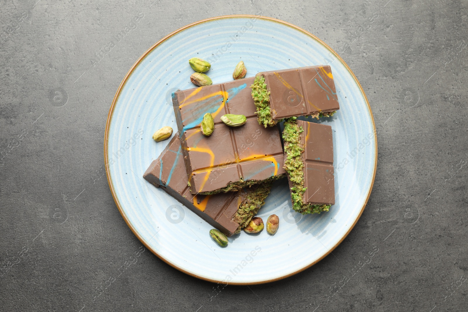 Photo of Pieces of Dubai chocolate bar with pistachios and knafeh on grey table, top view