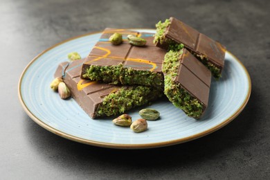 Photo of Pieces of Dubai chocolate bar with pistachios and knafeh on grey table, closeup