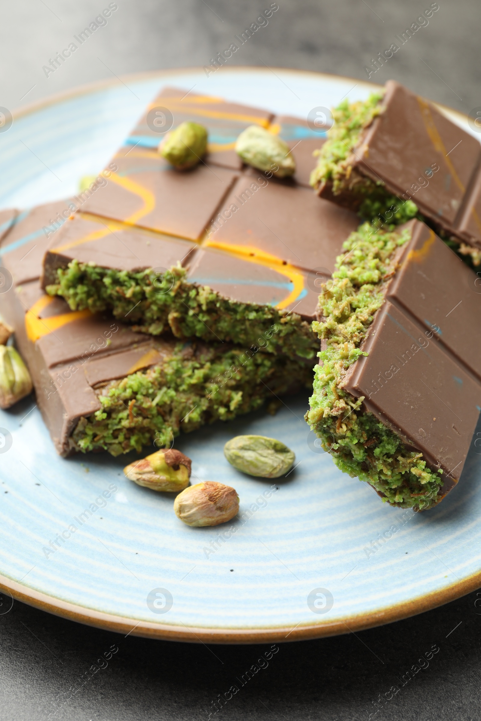 Photo of Pieces of Dubai chocolate bar with pistachios and knafeh on grey table, closeup