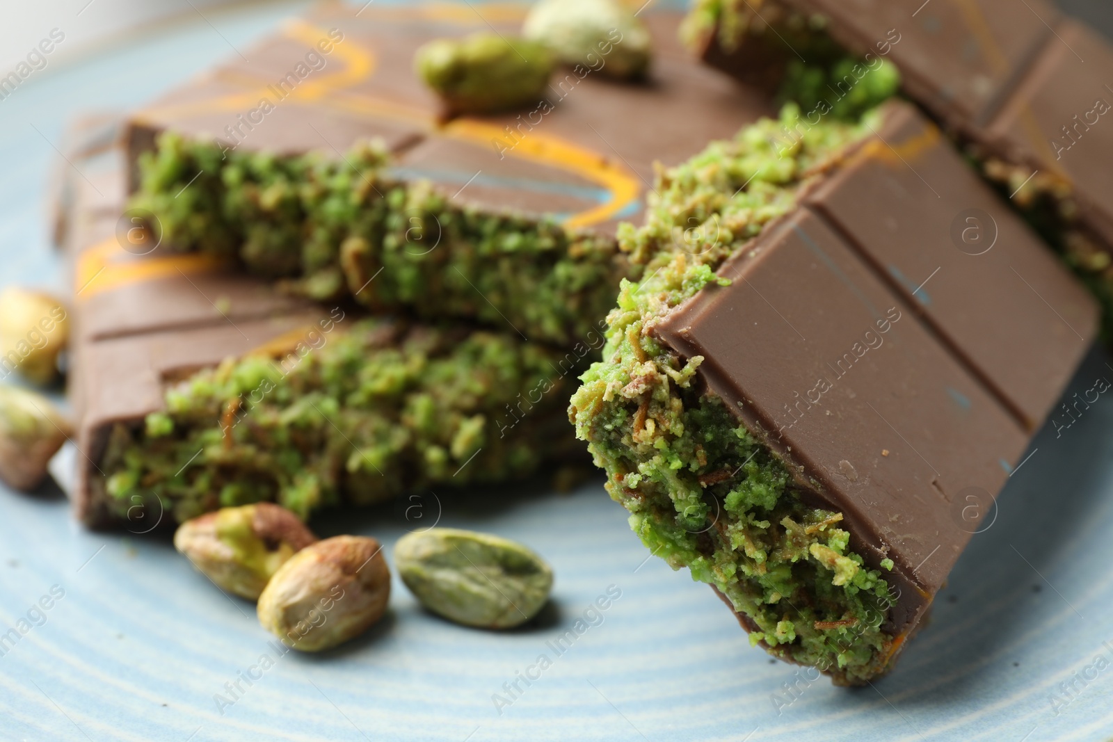 Photo of Pieces of Dubai chocolate bar with pistachios and knafeh on plate, closeup