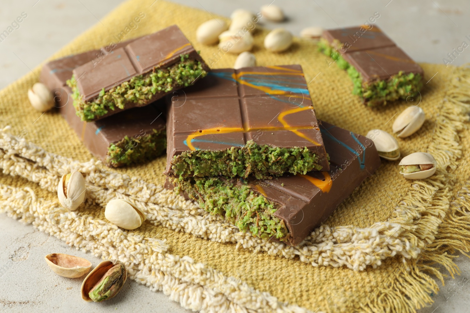 Photo of Pieces of Dubai chocolate bar with pistachios and knafeh on light table, closeup