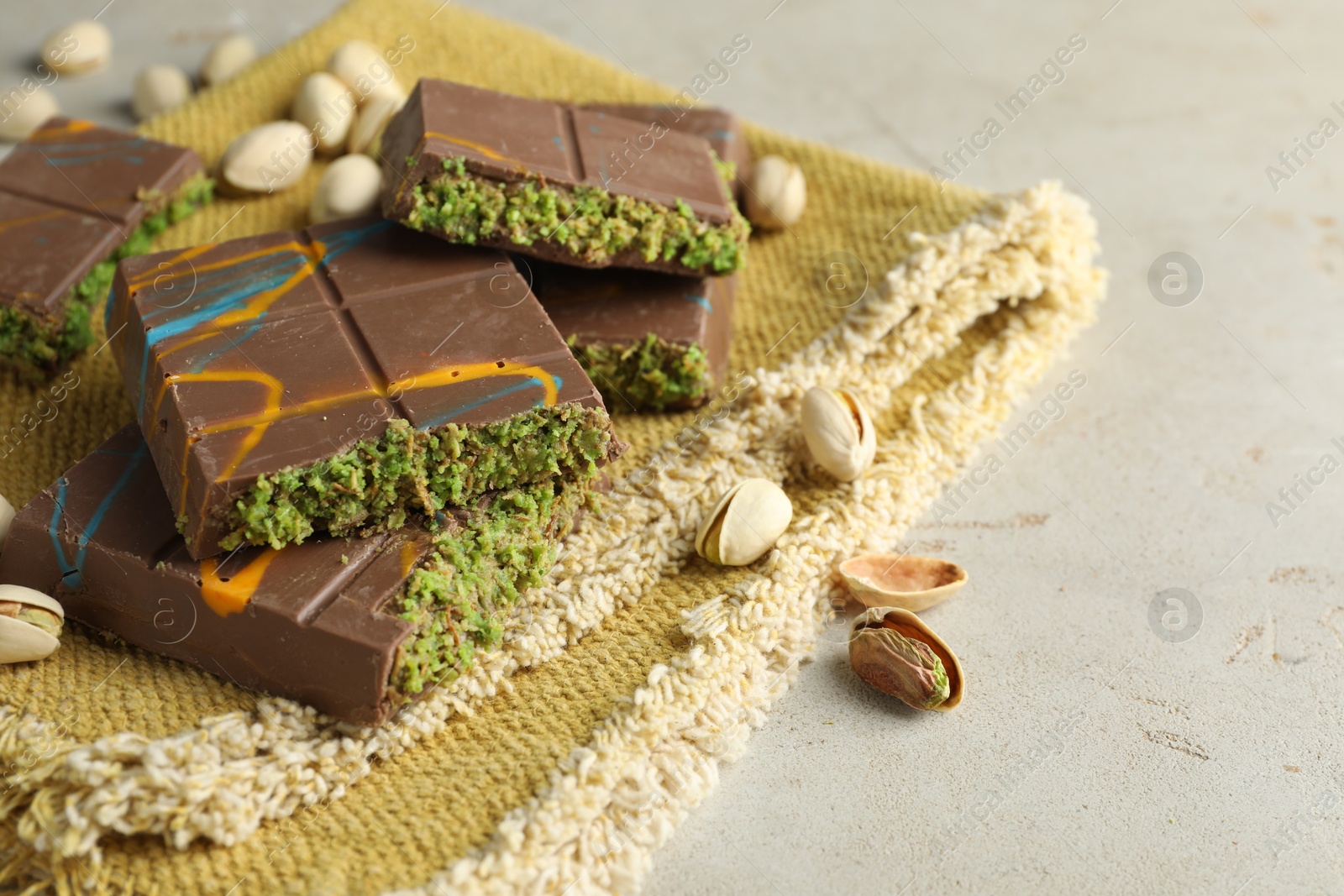 Photo of Pieces of Dubai chocolate bar with pistachios and knafeh on light table, closeup