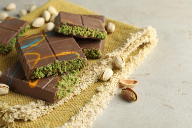 Photo of Pieces of Dubai chocolate bar with pistachios and knafeh on light table, closeup