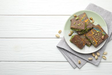 Photo of Pieces of Dubai chocolate bars with pistachios and knafeh on white wooden table, flat lay. Space for text