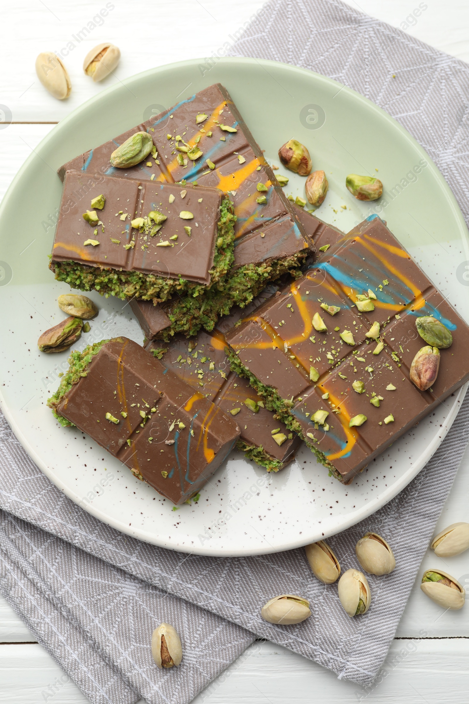 Photo of Pieces of Dubai chocolate bars with pistachios and knafeh on white wooden table, flat lay