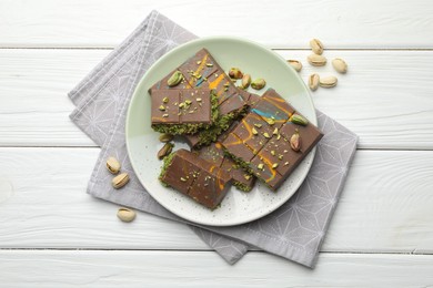 Photo of Pieces of Dubai chocolate bars with pistachios and knafeh on white wooden table, flat lay