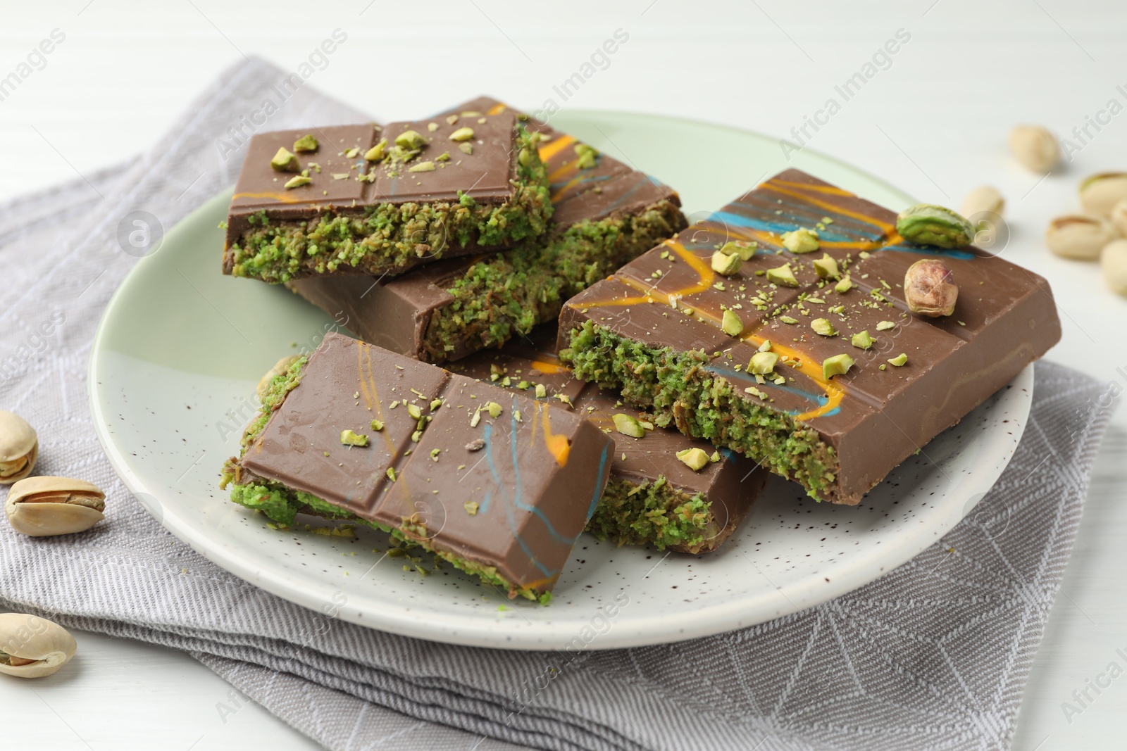 Photo of Pieces of Dubai chocolate bars with pistachios and knafeh on white wooden table, closeup