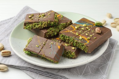 Photo of Pieces of Dubai chocolate bars with pistachios and knafeh on white wooden table, closeup