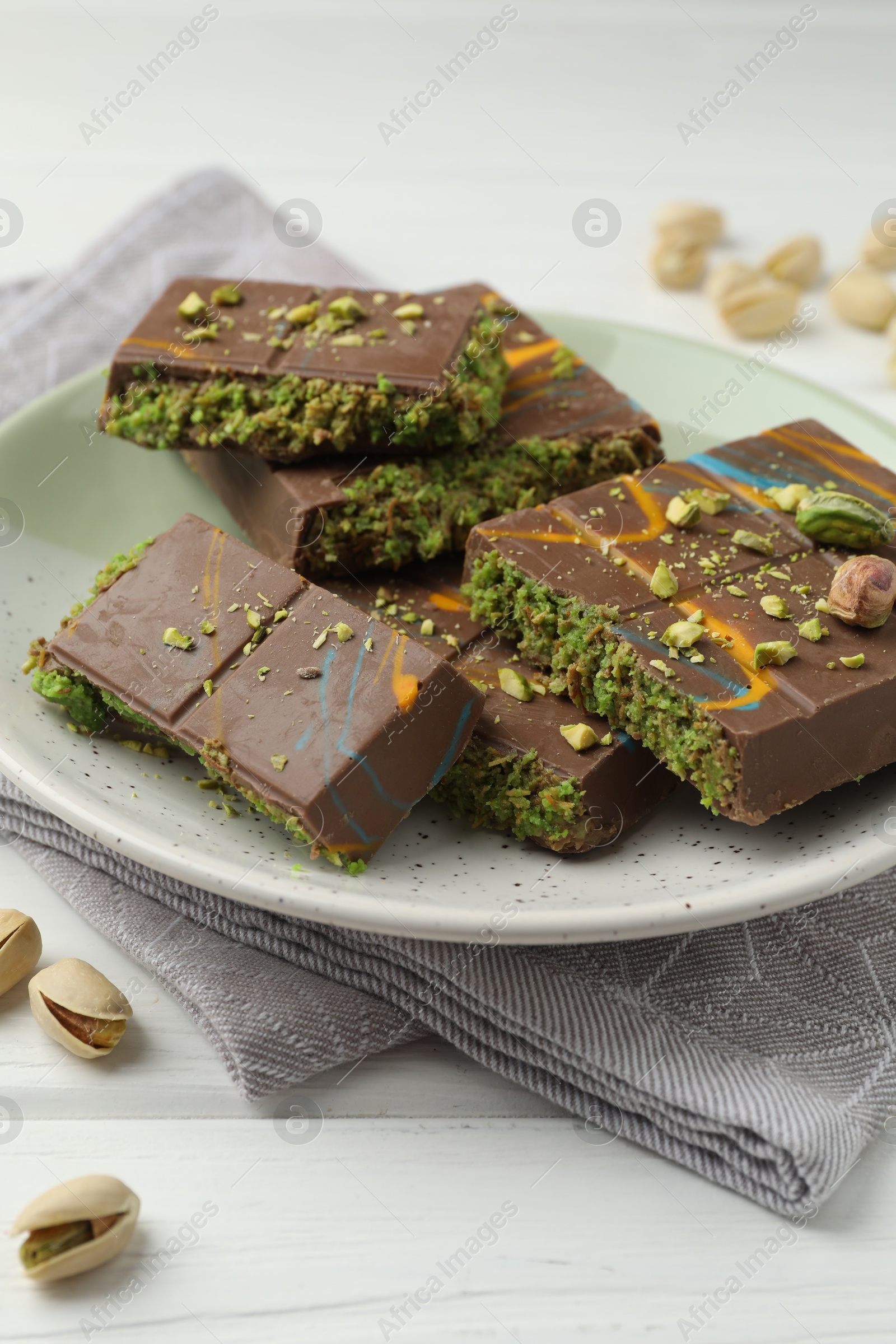 Photo of Pieces of Dubai chocolate bars with pistachios and knafeh on white wooden table, closeup