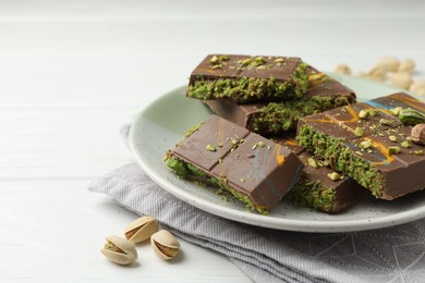 Photo of Pieces of Dubai chocolate bars with pistachios and knafeh on white wooden table, closeup. Space for text