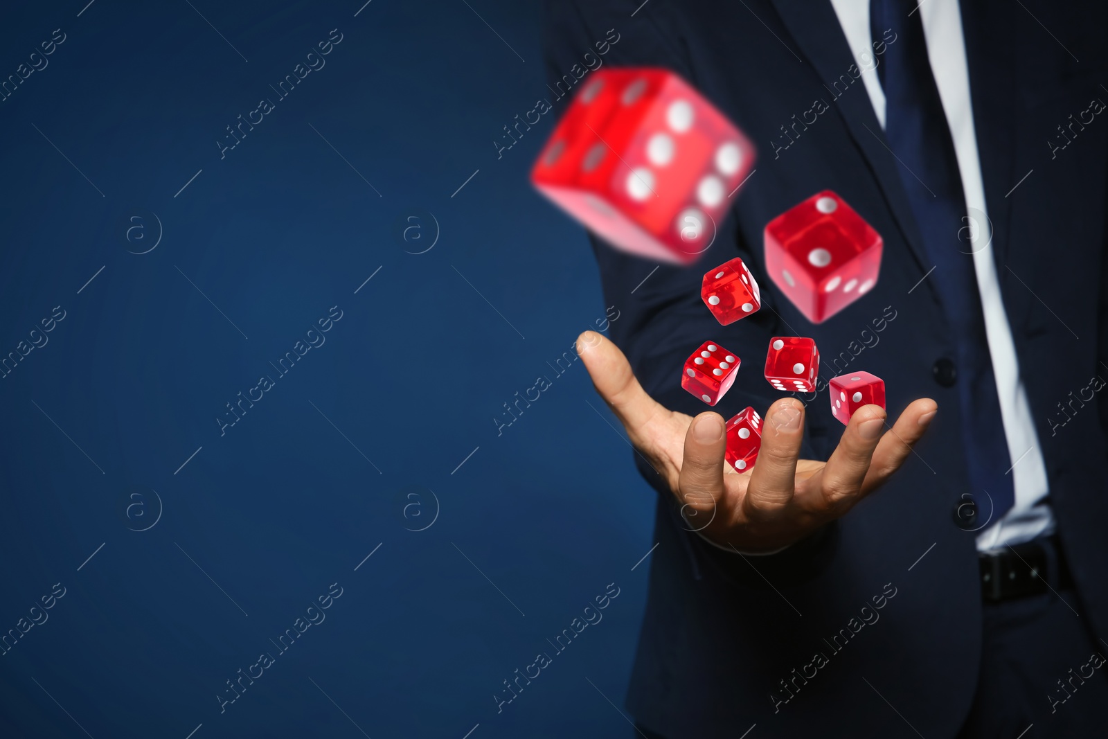 Image of Businessman throwing red dice on blue background, closeup. Space for text