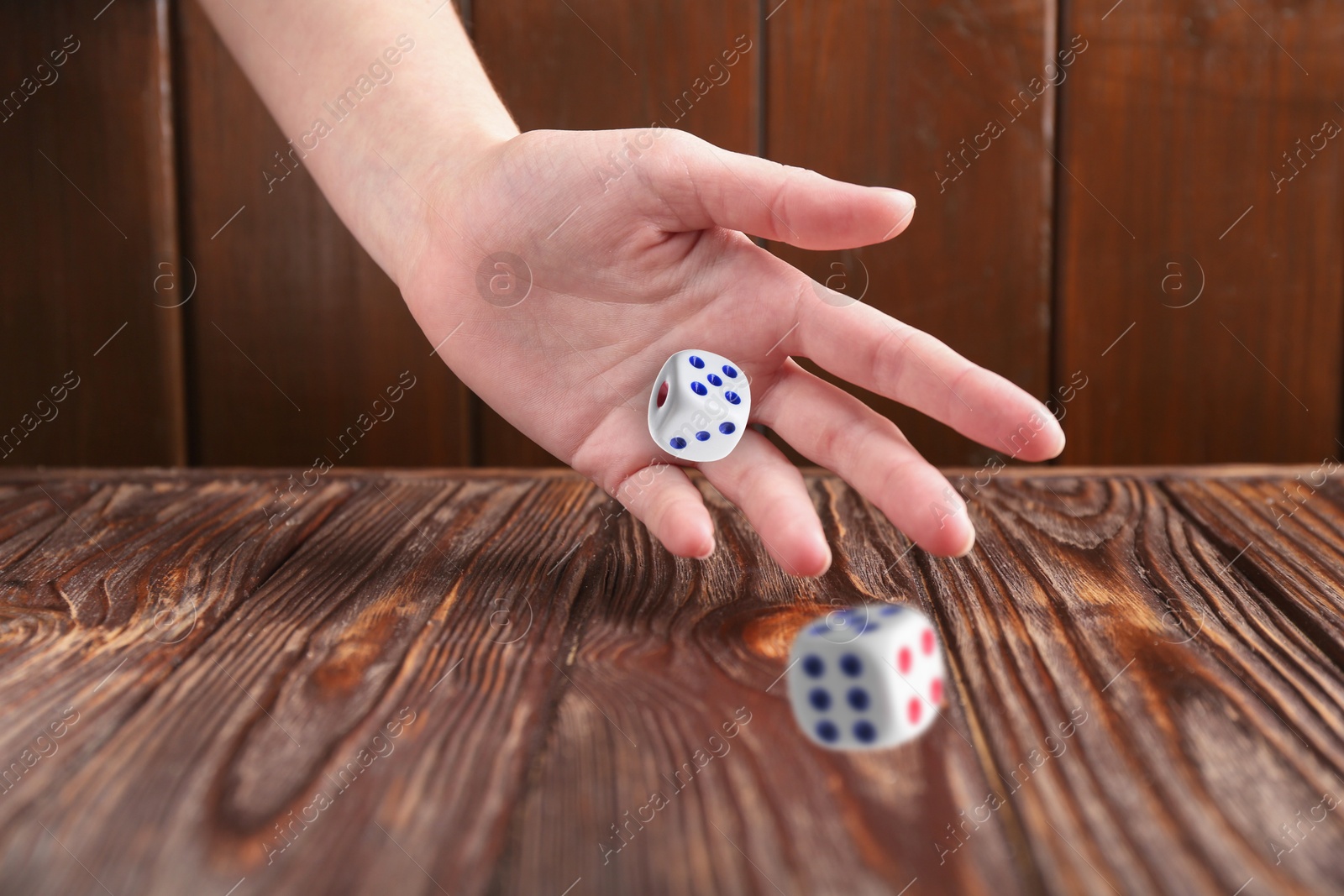 Image of Woman throwing white dice on wooden table, closeup