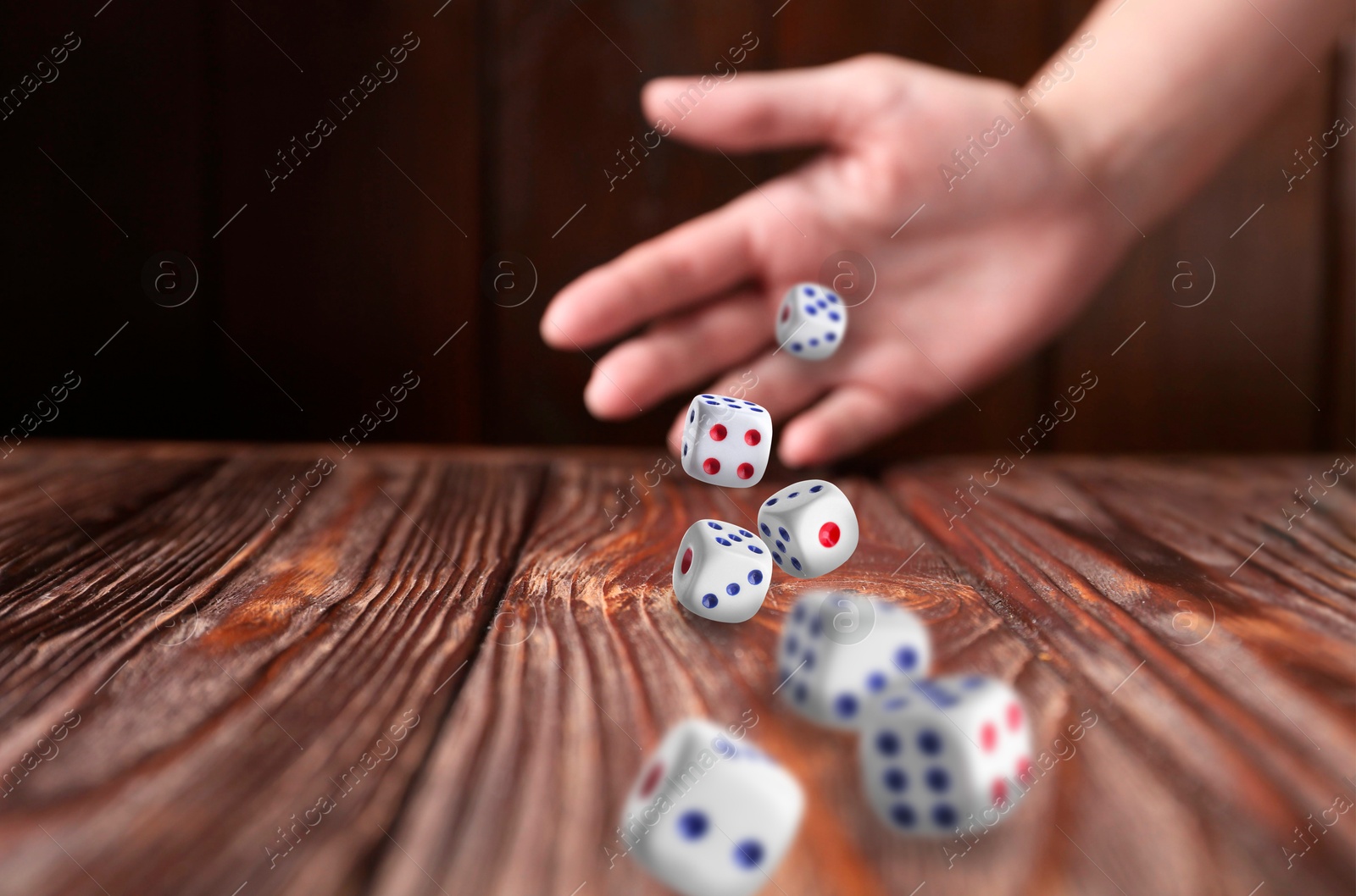 Image of Woman throwing white dice on wooden table, closeup. Space for text