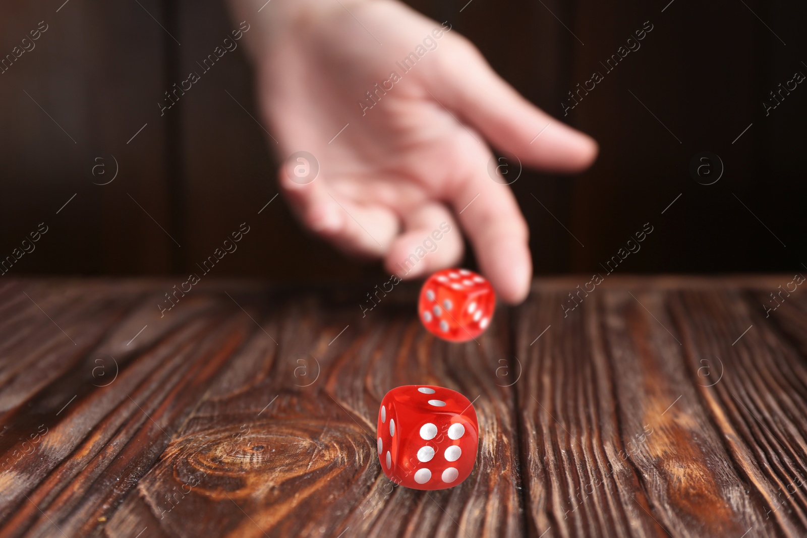 Image of Woman throwing red dice on wooden table, closeup