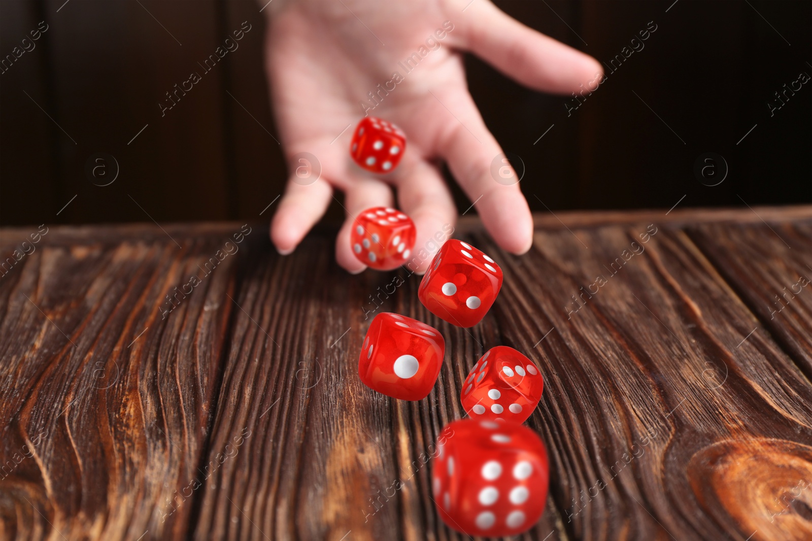 Image of Woman throwing red dice on wooden table, closeup