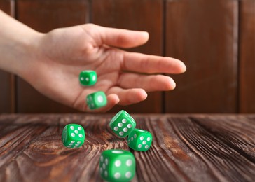 Image of Woman throwing green dice on wooden table, closeup