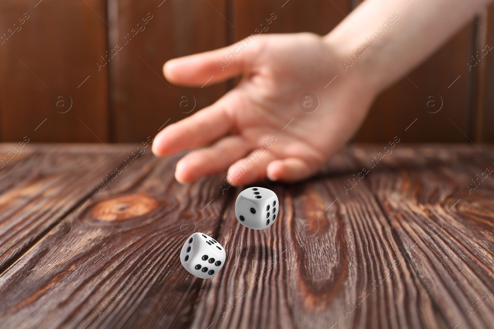 Image of Woman throwing white dice on wooden table, closeup