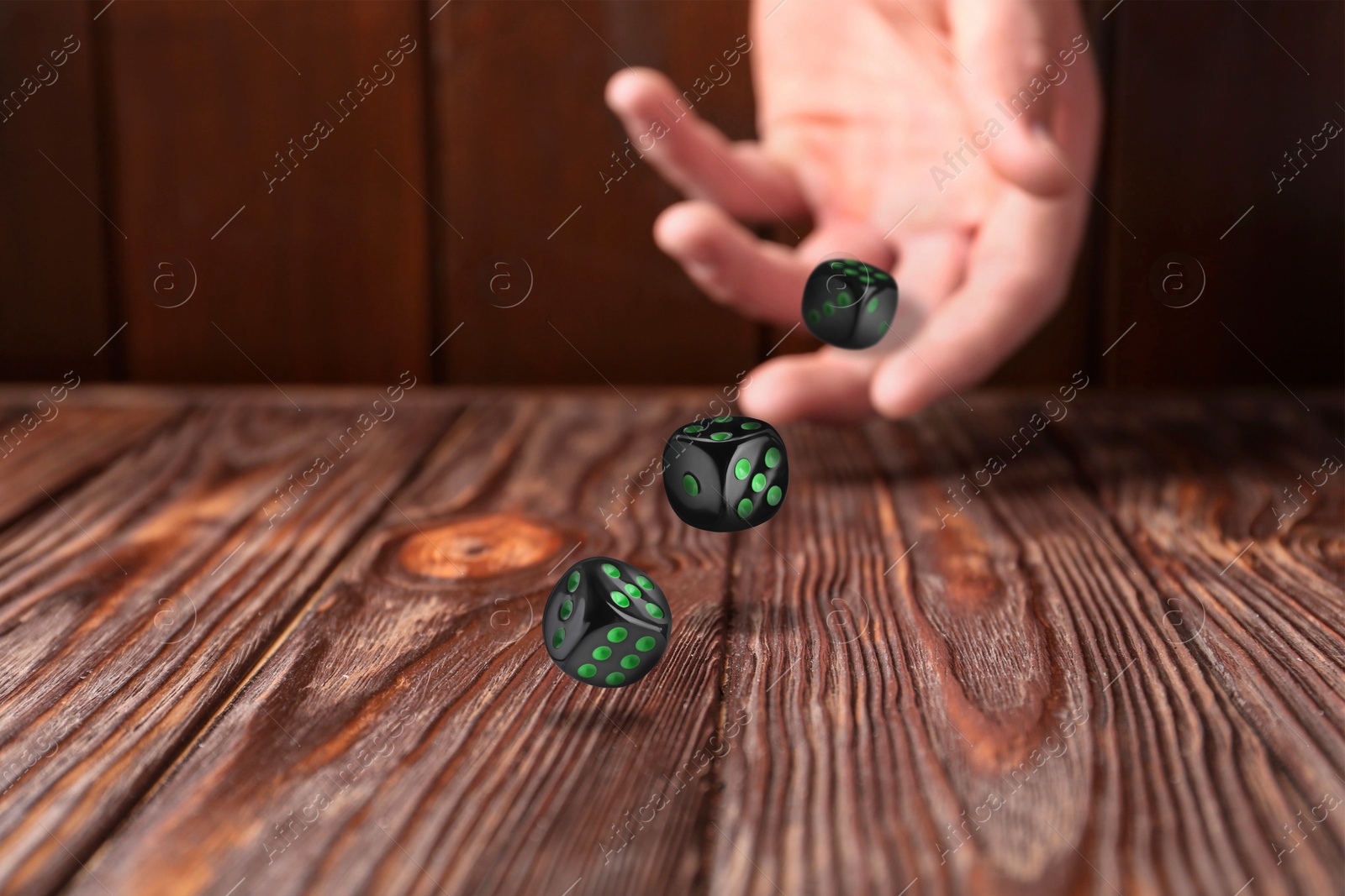 Image of Man throwing black dice on wooden table, closeup. Space for text