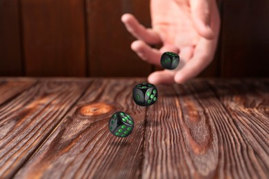 Image of Man throwing black dice on wooden table, closeup. Space for text