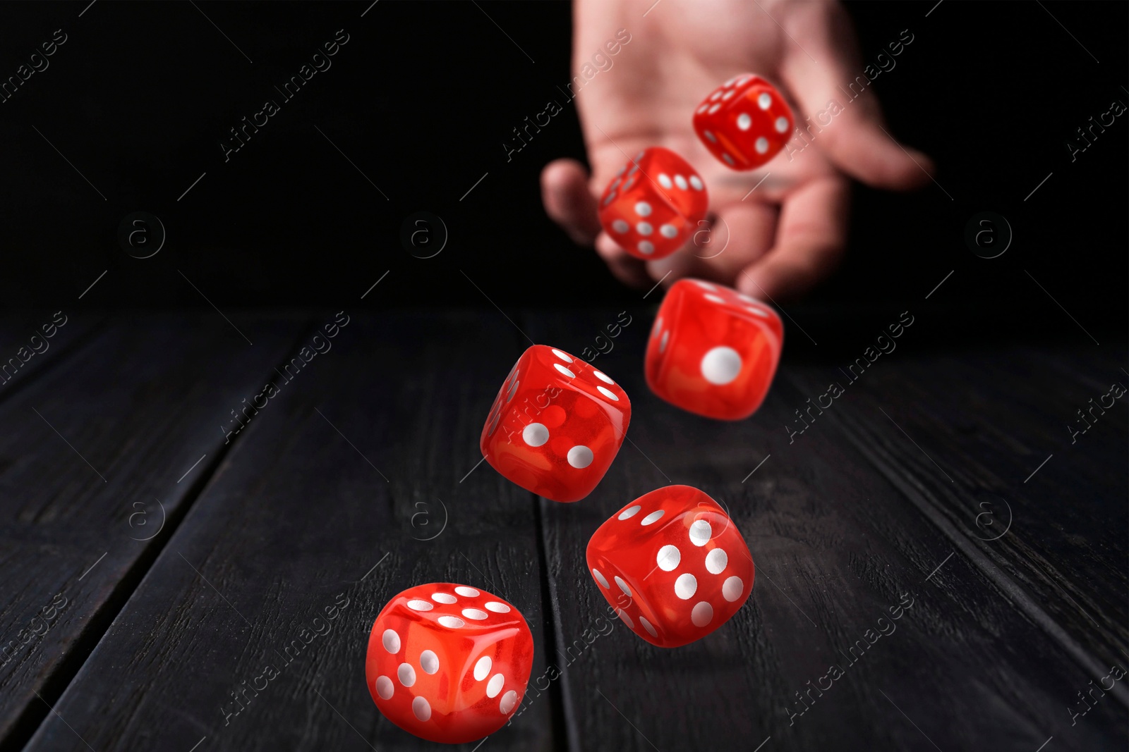 Image of Man throwing red dice on black wooden table, closeup. Space for text