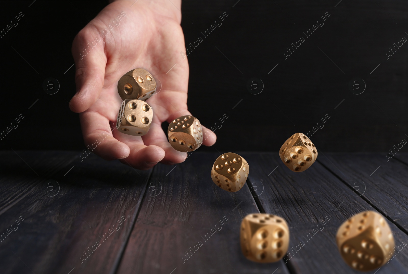 Image of Man throwing gold dice on black wooden table, closeup. Space for text