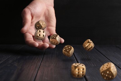 Image of Man throwing gold dice on black wooden table, closeup. Space for text